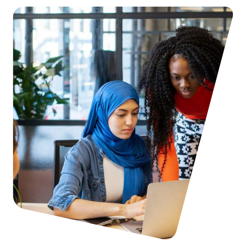 Tw woman leaning over computer in office discussing together